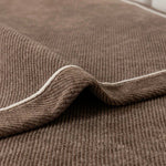 Close-up fold of brown luxurious chenille sofa cover showing cream contrast piping edge detail